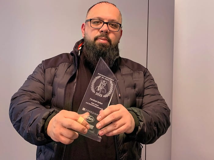 Farshad Safari tient le trophée de « l'agent de sécurité de l'année 2025 » dans ses mains et regarde la caméra.