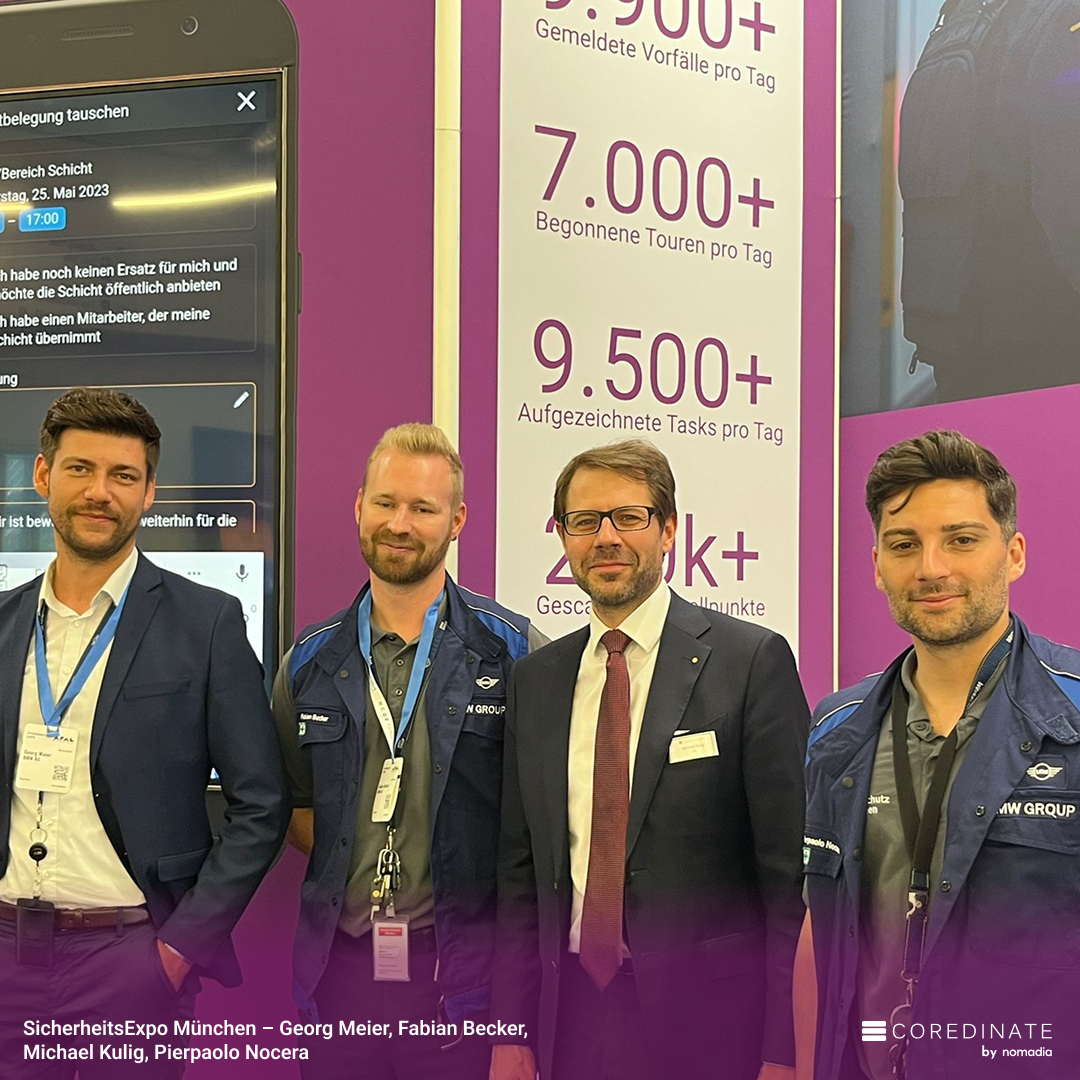 Vier Männer (Georg Meier, Fabian Becker, Michael Kulig, Pierpaolo Nocera) lächeln für ein Gruppenfoto auf der SicherheitsExpo München, vor einem lilafarbenen COREDINATE®-Messestand mit Zahlen zur Task-Statistik.