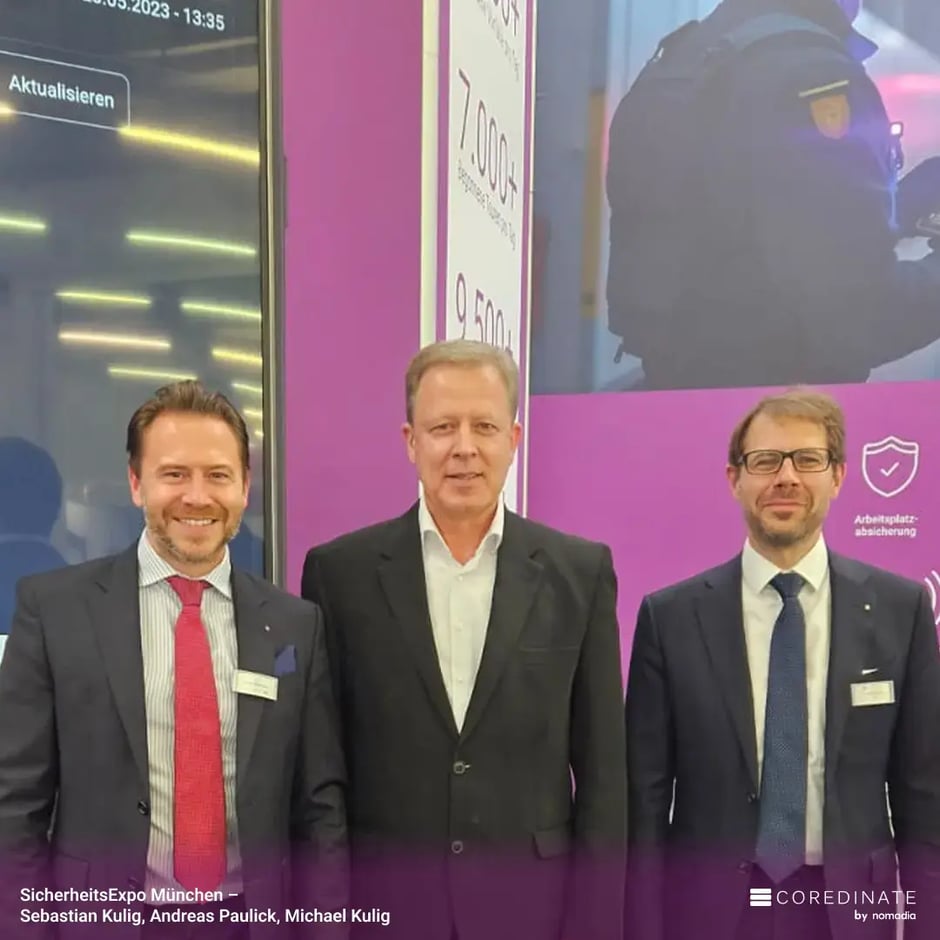 Sebastian Kulig, Andreas Paulick und Michael Kulig stehen nebeneinander und lächeln in die Kamera am COREDINATE®-Messestand auf der SicherheitsExpo München.