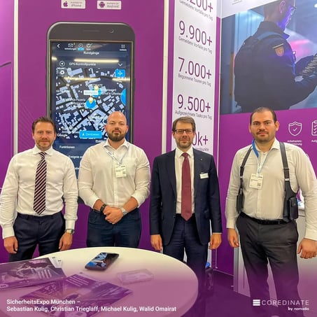 Sebastian Kulig, Christian Trieglaf, Michael Kulig und Walid Omairat stehen zusammen am COREDINATE®-Messestand auf der SicherheitsExpo München und blicken in die Kamera.