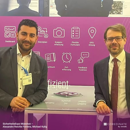 Alexandre Reiche Ferreira und Michael Kulig stehen nebeneinander am COREDINATE®-Messestand auf der SicherheitsExpo München und lächeln in die Kamera.