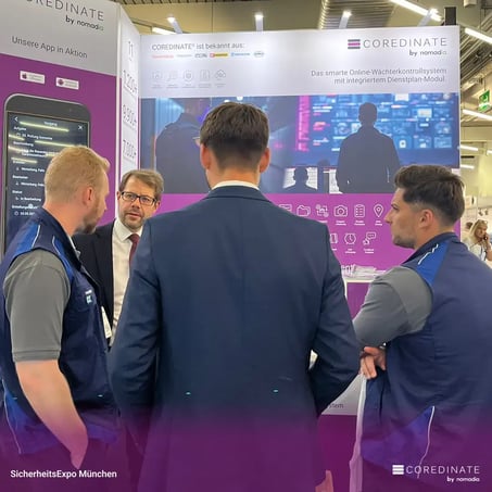 Vier Männer, darunter Michael Kulig, Georg Meier, Fabian Becker und Pierpaolo Nocera, stehen mit dem Rücken zur Kamera und sprechen am COREDINATE®-Messestand auf der SicherheitsExpo München.